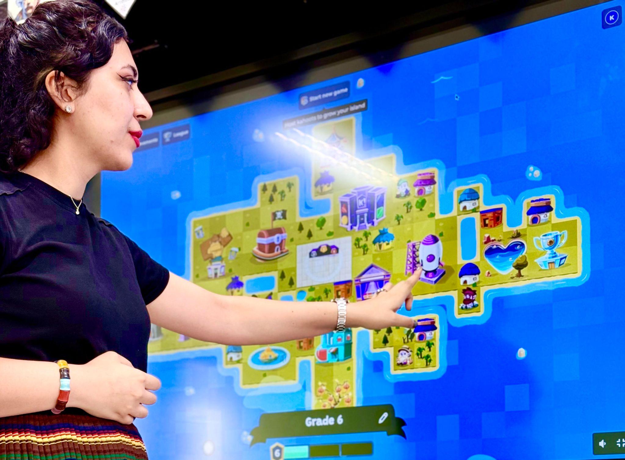 teacher in front of screen with kahootopia island displayed, pointing to screen